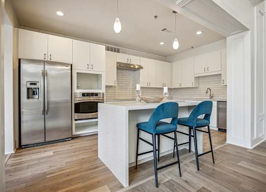 A kitchen with a refrigerator, oven, and two chairs.