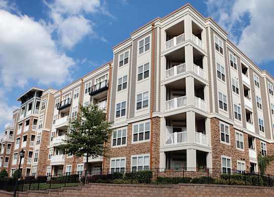 A large apartment building with balconies and a brick wall in front.