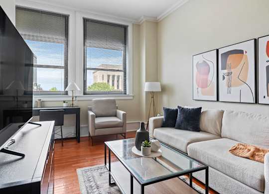 A living room with a grey couch, a glass coffee table, and a painting on the wall.