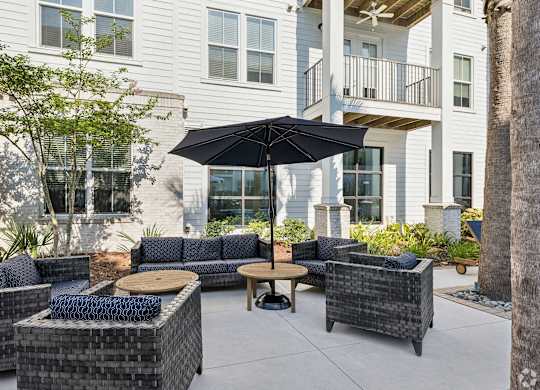 A patio with a black umbrella and wicker furniture.