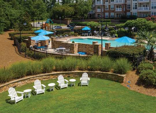 A pool surrounded by a grassy area with chairs and umbrellas.