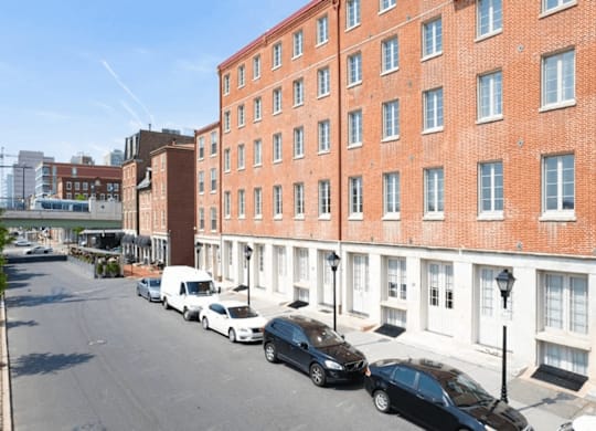 A street view of a row of red brick buildings with cars parked on the side.