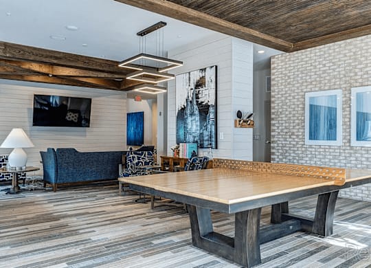 A large wooden table is in the middle of a room with a blue couch and a television mounted on the wall.