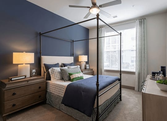 A bedroom with a four-poster bed, a ceiling fan, and a nightstand with a lamp.