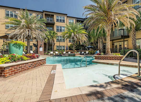 A pool surrounded by palm trees and a brick wall.