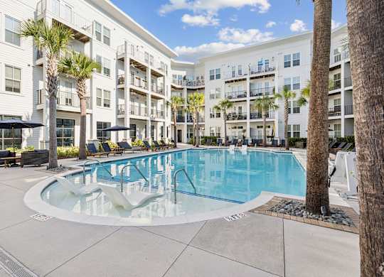 A large swimming pool is surrounded by palm trees and lounge chairs.