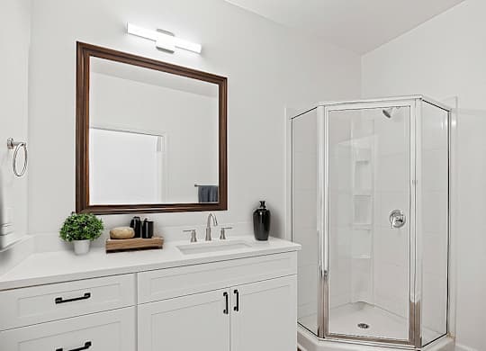 A white bathroom with a mirror, sink, and shower.