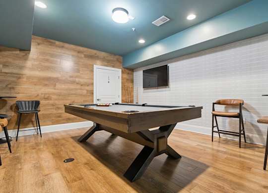 A pool table is in the middle of a room with a wooden floor and a white door.