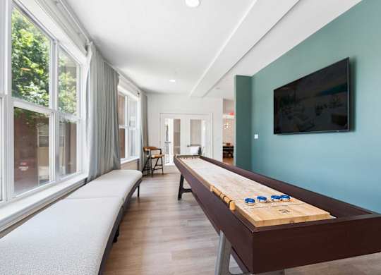 A shiny wooden table with blue cups on it sits in a room with a green wall and a television.