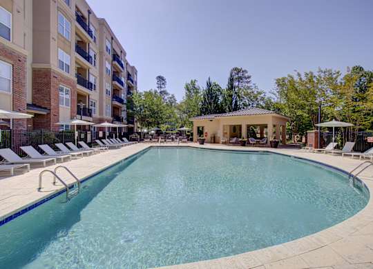 A large outdoor swimming pool surrounded by sun loungers and a building in the background.