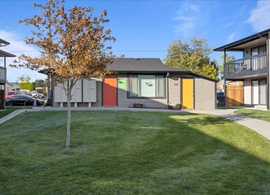 Leasing office exterior with large windows and an orange and yellow door. Green grass and a tree in front, and a parking lot behind the building. at Brix, Walla Walla, WA, 99362