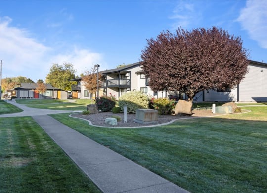 Side walk entering the community through green grass and large trees. Apartment buildings in the background. at Brix, Washington, 99362