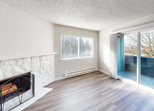 Sun-filled living area at Peak 88 Apartments Renton WA showcasing a fireplace, wood-style floors, and balcony views of trees.