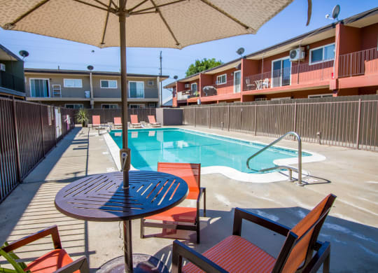 a pool with a table and chairs next to a resort style pool at Ella 1711 Apartments, Woodland, CA 95695