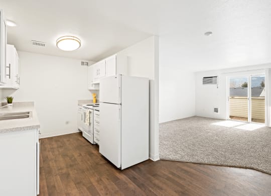 White kitchen with new cabinets, dark faux wood flooring, and view of living room area with taupe carpet and sliding glass door in the distance. at North Pointe, Post Falls, ID 83854