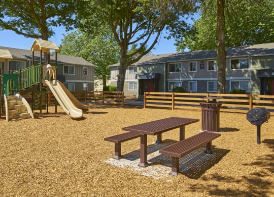 a playground with a slide and a picnic table in front of apartments  at Woodhaven, Everett, Washington