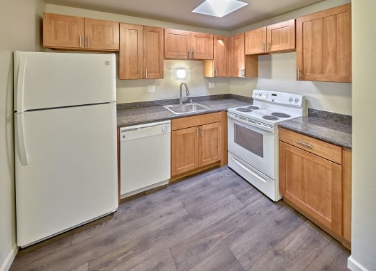 L shaped kitchen with white appliances, light brown cabinets and wood style flooring.at Park View Apartments, Wenatchee