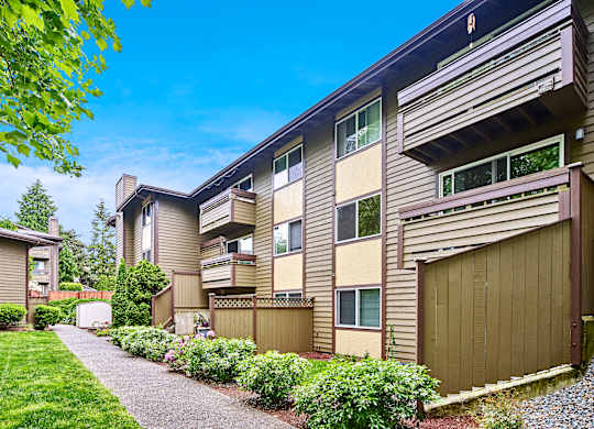 Exterior view of personal patios or balconies, manicured grounds and building, and blue skies in the background at Heritage Grove, Renton, WA.