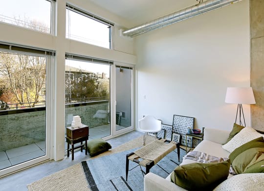 Living room with concrete flooring, floor to ceiling windows and a private outdoor patio. Inside is staged with a coffee table, rug and chair.at 19th & Mercer, Washington