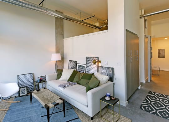 Apartment living room with staged couch, coffee table and rug. Concrete flooring and tall ceilings.at 19th & Mercer, Seattle, WA