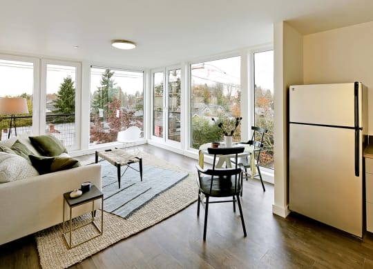 Living room with floor to ceiling windows with city and tree views. Staged with a couch, coffee table, rug and chair.at 19th & Mercer, Seattle Washington