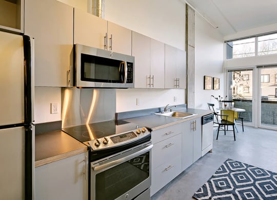 Kitchen with a fridge, oven, microwave, sink and dishwasher from left to right. Stainless steel appliances and a staged seating area.at 19th & Mercer, Seattle Washington