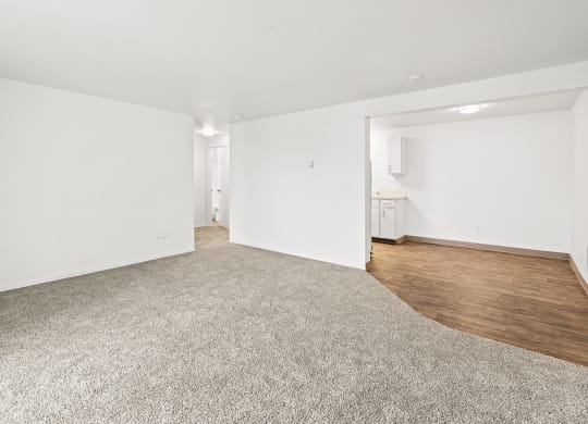 Bright white living room area with taupe carpet, and view of dining area with faux wood flooring at the far right back of the photo.at North Pointe, Post Falls, ID