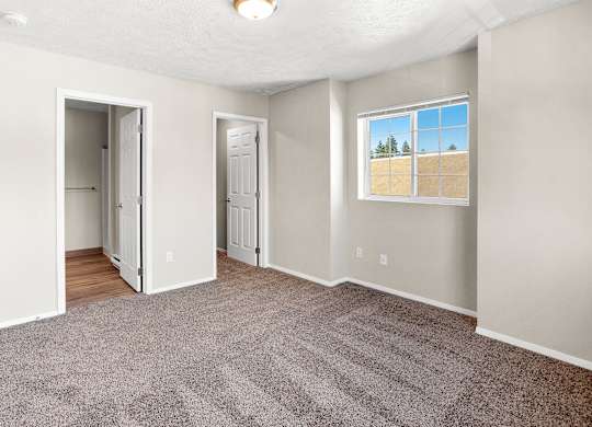 Carpeted bedroom with a large window overlooking an open field at The Overlook at Falls Park Apartments in Post Falls, ID.
