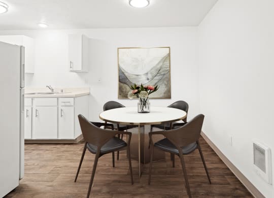 A dining area with hardwood floors and access to the kitchen. Staged with a round table, 4 chairs, and wall art.at North Pointe, Post Falls, ID 83854