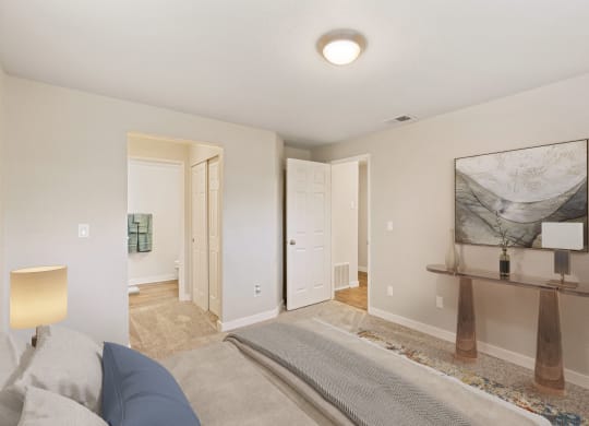 Bedroom with hallway door and door to en suite bathroom, staged bed, carpet, side tables and art on walls.at Capitol Crossing, Olympia