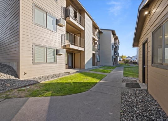 A large sidewalk entering Brix Apartments on a blue sky day. Grass aligns the sidewalk and apartments with balconies. at Brix, Walla Walla, WA, 99362