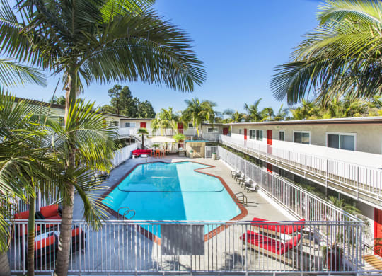 Outdoor swimming pool with sun chairs, a lounge area lined with apartments, and palm trees at Pacific Sands, San Diego, CA