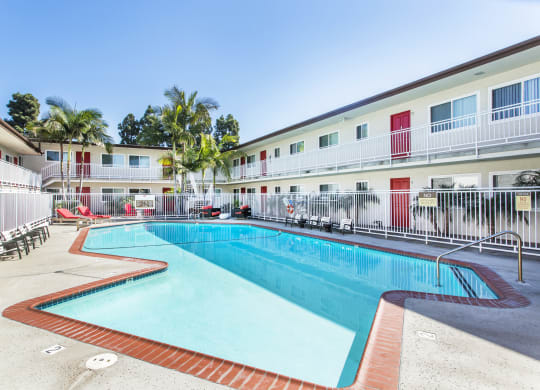Outdoor swimming pool with sun chairs, a lounge area lined with apartments, and palm trees at Pacific Sands, San Diego, CA