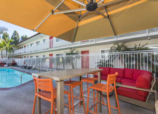 Outdoor Lounge area with table, bar stools and couch. Swimming Pool is several feet away from the lounge at Pacific Sands, San Diego, 92117