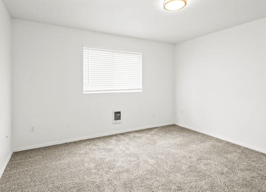 Bright empty bedroom with taupe carpet, white walls and white horizontal blinds on a window on the opposite wall.at North Pointe, Idaho, 83854