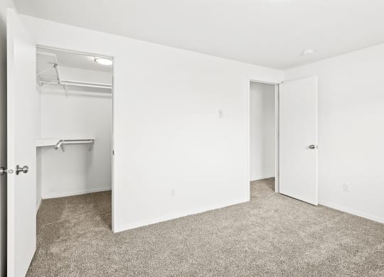 Bright white bedroom with taupe carpet and two open doors. One door leading to hallway, one door leads to walk-in closet with rods at multiple levels.at North Pointe, Idaho