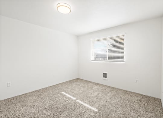 Bright empty bedroom with taupe carpet, white walls and white horizontal blinds on a window on the opposite wall.at North Pointe, Idaho, 83854