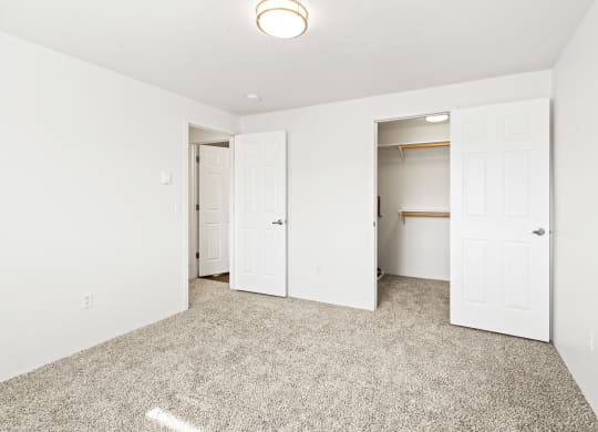 Bright white bedroom with taupe carpet and two open doors. One door leading to hallway, one door leads to walk-in closet with rods at multiple levels.at North Pointe, Post Falls Idaho