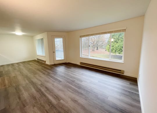 Spacious living room with wood-like flooring, an oversized window with nature views, and a door to a private balcony.at The Trail, Snohomish