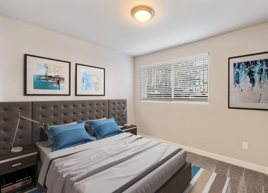 Bedroom with large window, staged bed, carpet, side tables and art above bed.at Capitol Crossing, Olympia
