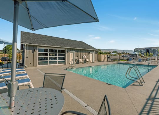 Bright blue pool with lounge chairs, umbrella-covered seating, and a view of the clubhouse. at Altitude, East Wenatchee, WA, 98802