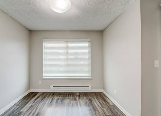 A dining room with taupe walls, wood-like flooring, a large window with blinds on the back wall, and overhead lighting. at Pointe East, Washington, 98424