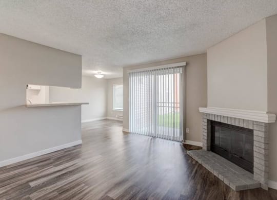 A living room with a fireplace, sliding glass doors to a patio, a kitchen breakfast bar, and a dining room to the left. at Pointe East, Fife, Washington
