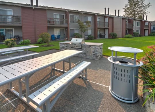 BBQ and picnic area with two picnic tables, a stainless steel BBQ, and a large green lawn and landscaping behind. at Pointe East, Fife, WA, 98424