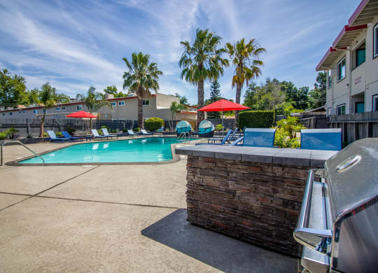 Woodland Village pool and BBQ with stone countertop looking out to pool and palm trees at Woodland Village Apartments , California