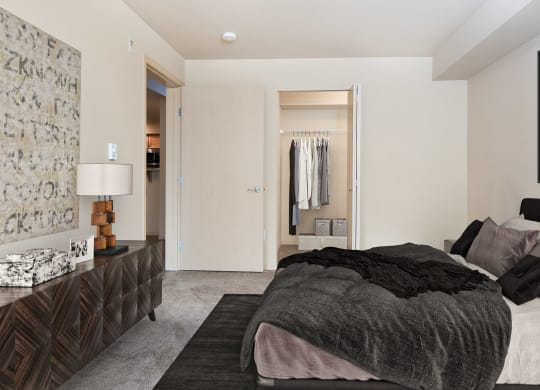 Carpeted bedroom with a queen size bed, a long set of drawers, art on the walls, and a closet with an accordion door at 6 Wood Flats, Lacey, WA
