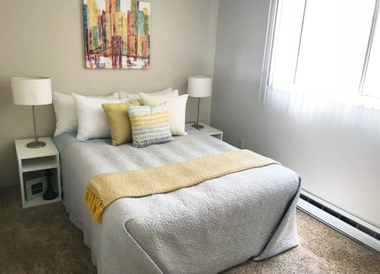 Bedroom with queen sized bed and large window with blinds. Staged with bed, side table, lamp and wall art.at The Lakes Apartments, Moses Lake, 98837