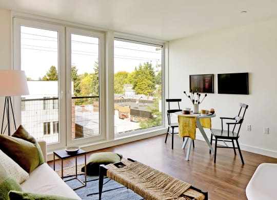 Living room with floor to ceiling windows with city and tree views. Staged with a couch, coffee table, rug and chair.at 19th & Mercer, Seattle Washington