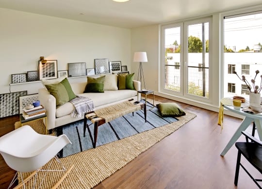 Living room with floor to ceiling windows with city and tree views. Staged with a couch, coffee table, rug and chair.at 19th & Mercer, Seattle Washington