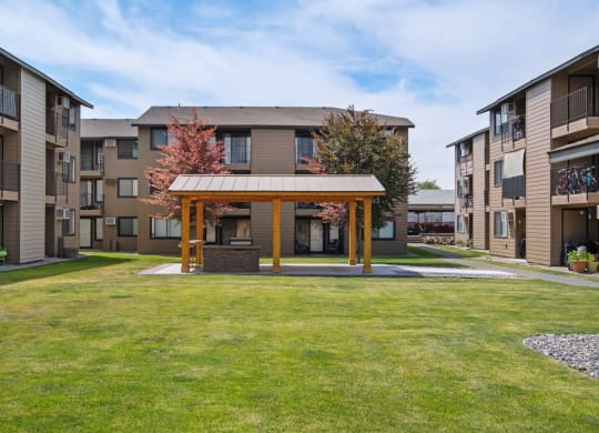 The Brix community courtyard surrounded by grass, trees, and apartments with a covered structure for residents in the center. at Brix, Washington, 99362